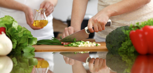 Closeup of human hands cooking in kitchen. Mother and daughter or two female friends cutting vegetables for fresh salad. Friendship, family dinner and lifestyle concepts
