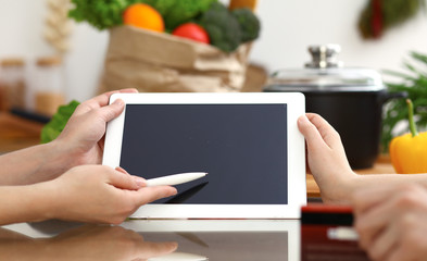 Close-up of human hands using tablet or touch pad. Two women in kitchen. Cooking, friendship or online shopping concepts