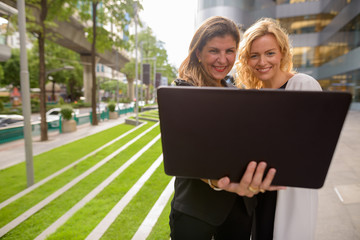 Portrait of two happy businesswoman using laptop computer together outdoors