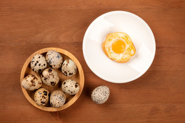 A photo of quail eggs, shot from the top on a dark rustic wooden background with an egg cooked sunny side up and a place for text