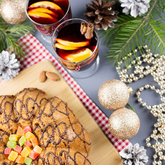 Tasty Christmas cookies, hot mulled wine and decorations with Christmas tree and lights on black background.