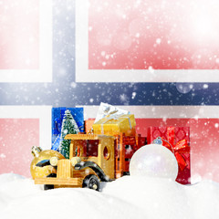 Christmas background.Toy truck with gifts, New Year fir, balls in the snowdrift and Norwegian flag