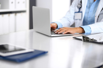 Unknown doctor woman typing on laptop computer while sitting at the desk in hospital office. close-up of hands. Physician at work. Medicine and health care concept