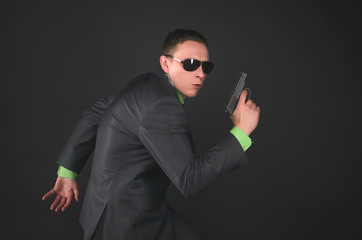 Security agent man with a gun in hand is walking on tiptoe isolated on black background.