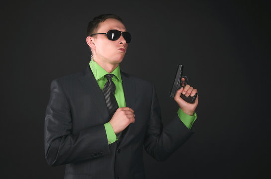 Arrogant security agent is posing with a gun in hand like a super spy isolated on black background.