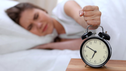 Alarm clock opposite of sleepy young woman stretching hand to ringing alarm willing turn it off....