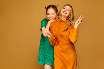Two young beautiful blond smiling hipster girls posing in trendy summer clothes. Carefree women isolated on golden background. Positive models going crazy and hugging