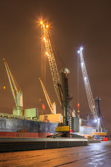 Fototapeta na wymiar Night scene with cranes on illuminated quay loading a moored vessel, Port of Antwerp, Belgium.