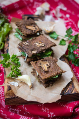 Crispy rye and flax seeds breads dehydrated and stuffed with fresh green salad leaves, mushrooms and Arabian hummus spread paste. Vegan, vegetarian snack on Christmas red tablecloth background.
