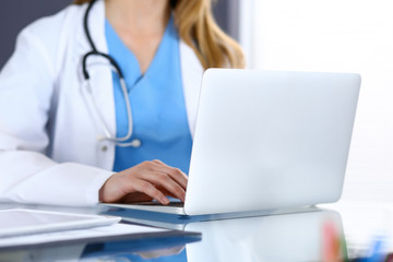 Doctor typing on laptop computer while sitting at the glass desk in hospital office. Physician at work. Medicine and healthcare concept