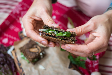 Crispy rye and flax seeds breads sandwich dehydrated and stuffed with fresh green salad leaves, mushrooms and hummus spread paste. Vegan, vegetarian snack on Christmas red tablecloth background. 