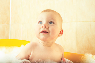 Little baby takes a bath in a yellow bath with bubbles and foam. The concept of happy child, love for bathing