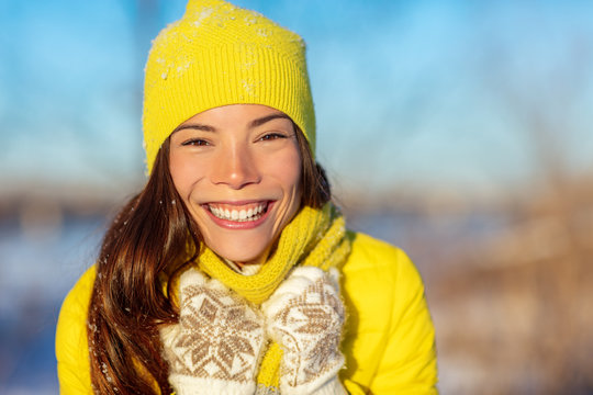 Winter Asian woman smiling in cold weather fashion accessories for winter: yellow hat and knit scarf, wool gloves, down jacket. Happy girl enjoying season outside.