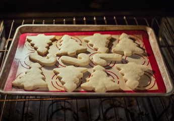 Christmas shaped sugar cookies baking in an oven. Selective focus on the cookies baking on the baking sheet