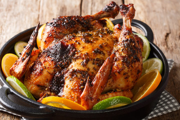 Citrus whole baked chicken served with fresh oranges and limes close-up in a frying pan. horizontal