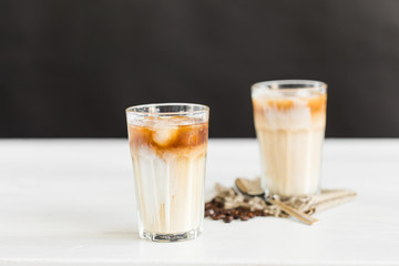 Ice coffee in a glass with cream over and coffee beans on the table