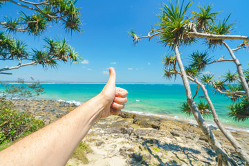 Fototapeta na wymiar A thumbs up hand sign at Noosa National Park on a perfect day with blue water and pandanus palms on the Sunshine Coast in Queensland