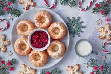 Mini bundt cakes with red whortleberry jam on light textured background with fir twigs, berries, cookies and candy canes