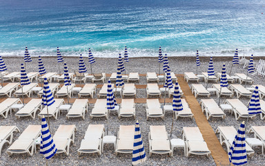 Vacant beach beds and umbrellas on mediterranean beach of Nice, France with blue water.