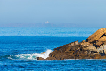 Sea waves breaking on a rocks. Deep blue sea waves hit cliff, hit rocks cliff. Mighty sea waves breaking on a cliff, splashing over rocks. Strong ocean waves hitting rocks