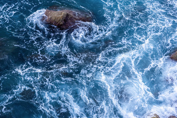 Moving wave and blue water of mediterranean sea touching rock beach making some small white bubble on surface.