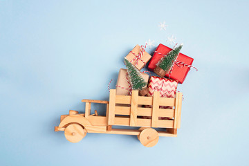 Wooden toy truck  with gift boxes and Christmas trees on blue background.