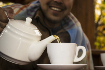 a man covered with a blanket pouring tea into a cup in the summerhouse on late Autumn 