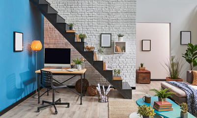 Decorative living room, loft style, working desk and desktop, black stairs and brick wall background.