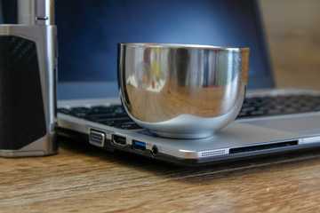 Coffee on modern laptop - ultrabook on wooden table with mobile phone and electronic cigarette