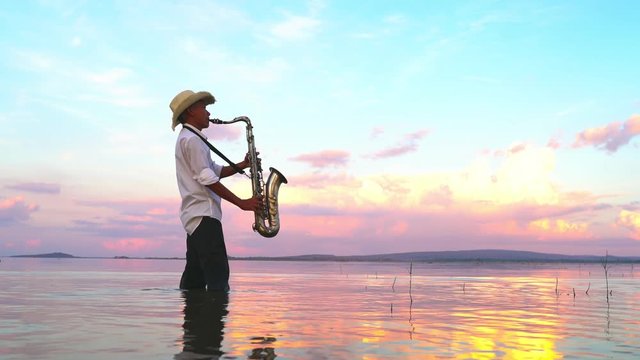 Man playing saxophone on river with sky background