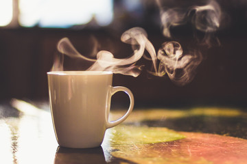 Close up of steaming cup of coffee or tea on vintage table - early morning breakfast on rustic...