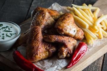 Barbecue grilled chicken wings close up with fries, tomato ketchup sauce and beer on wooden background. Meat food concept. 