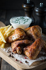 Barbecue grilled chicken wings close up with fries, tomato ketchup sauce and beer on wooden background. Meat food concept. 