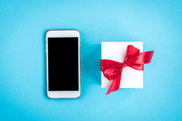Mobile phone and gift box with red bow on blue background.