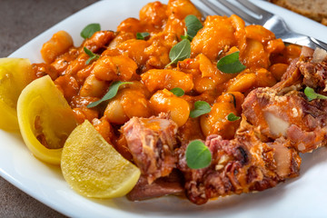 Beans stew with pork ribs and pickles on a white plate - close up view