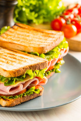 Close-up of two sandwiches with bacon, salami, prosciutto and fresh vegetables on rustic wooden cutting board. Club sandwich concept.