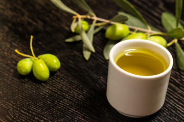 Branch of olive tree with green olive berries and cap of fresh olive oil on a black wooden table or board. Toned
