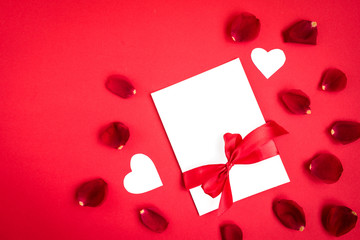 Greeting card with red bow and rose petals on red background.