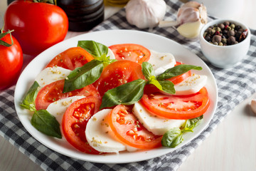 Photo of Caprese Salad with tomatoes, basil, mozzarella, olives and olive oil on wooden background. Italian traditional caprese salad ingredients. Mediterranean, organic and natural food concept.