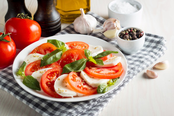 Fototapeta na wymiar Photo of Caprese Salad with tomatoes, basil, mozzarella, olives and olive oil on wooden background. Italian traditional caprese salad ingredients. Mediterranean, organic and natural food concept.