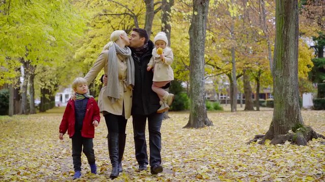 loving man and woman are kissing in city park, strolling and resting with kids in autumn day