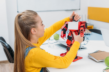 schoolgirl touching red handmade robot on desk in stem education class