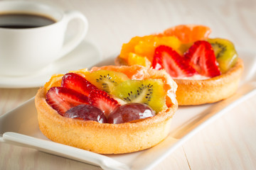 Photo of a fruit and berry tart dessert with toss sugar on wooden background. Fresh delicious sweet cake with raspberries, grapes, strawberries, cherry, kiwi, grapefruit and cream.