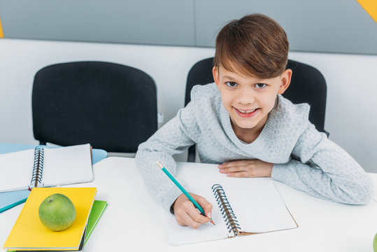 happy schoolboy writing in notepad in classroom - Powered by Adobe