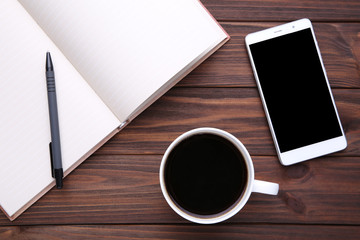 Smart phone with notebook and cup of coffee on brown wooden background