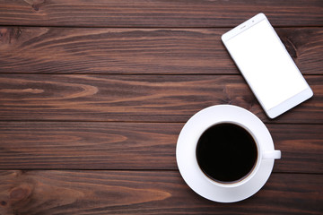 Smart phone with cup of coffee on brown wooden background