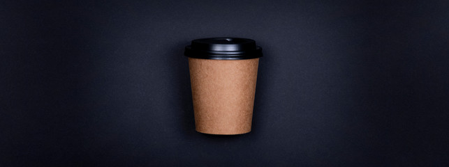 Single brown craft paper cup of coffee to go on black background with copy space.