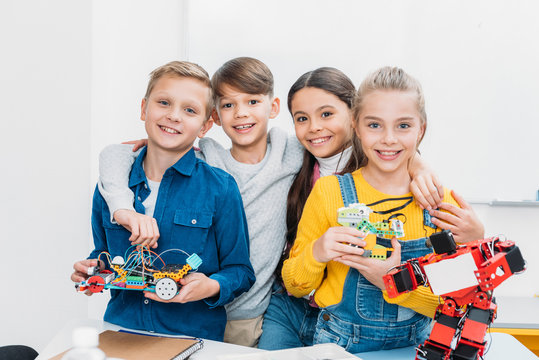 smiling schoolchildren standing, holding electric robots and looking at camera in stem class