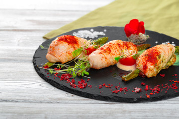 Asparagus rolled with chicken meat slices served on dark plate