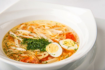 Homemade noodle soup with dill, quail eggs close-up on a white plate